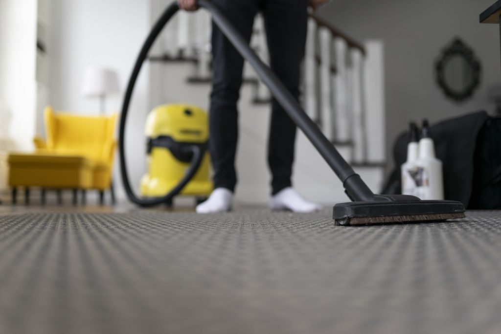 Man vacuuming the carpet in the room. House cleaning process